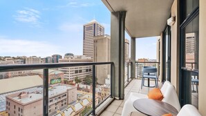 A balcony with a city view, white chairs, a table, and orange cushions. - Mantra Sydney Central (Haymarket)