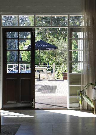 A wooden deck with a patio umbrella, a white fence, and a view of greenery through large windows.