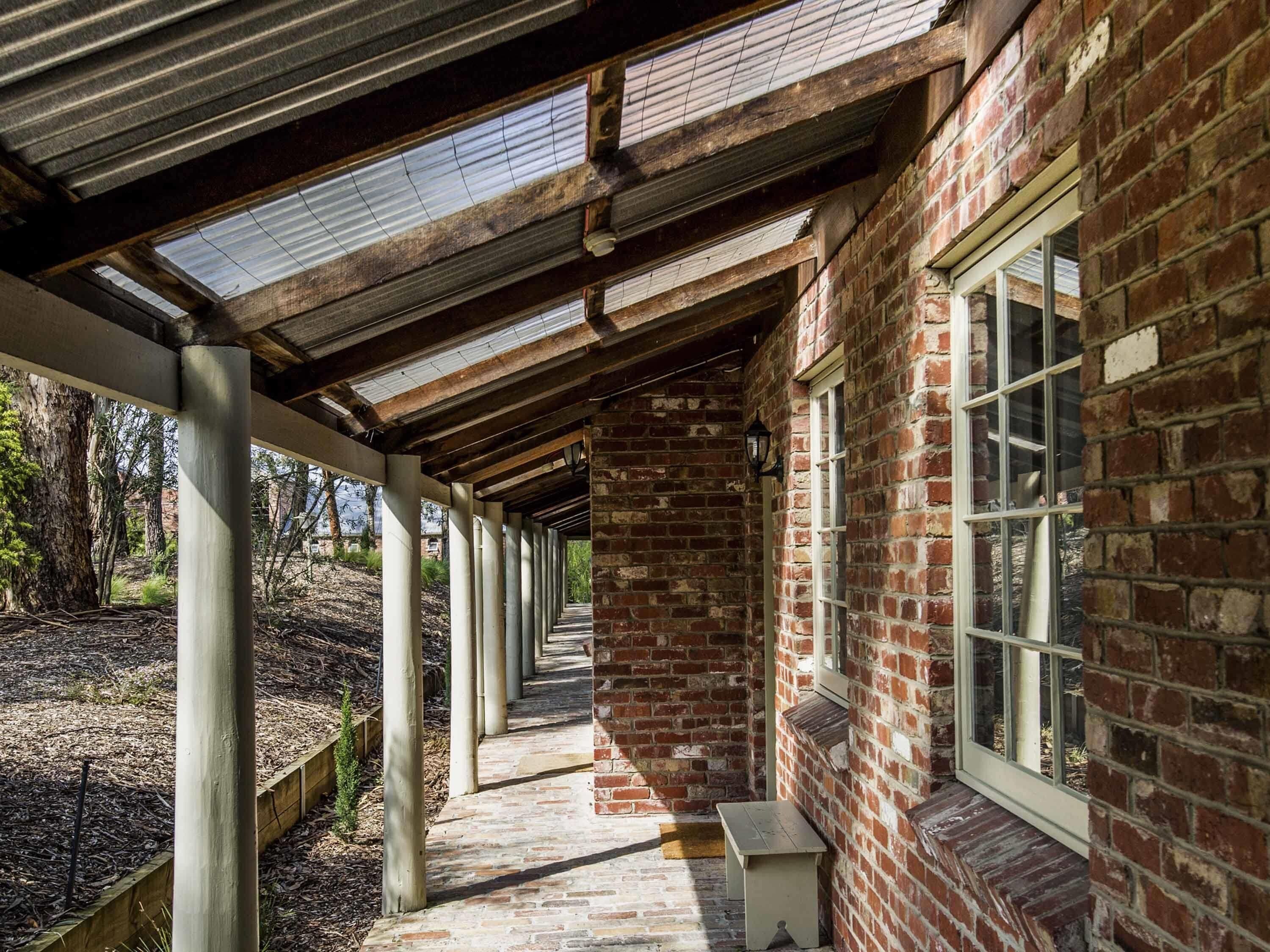 A covered outdoor area with a brick wall, windows, and a pathway.