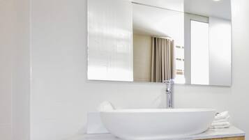 A modern bathroom with a large white vessel sink, a wooden vanity, and a mirror with a geometric pattern.