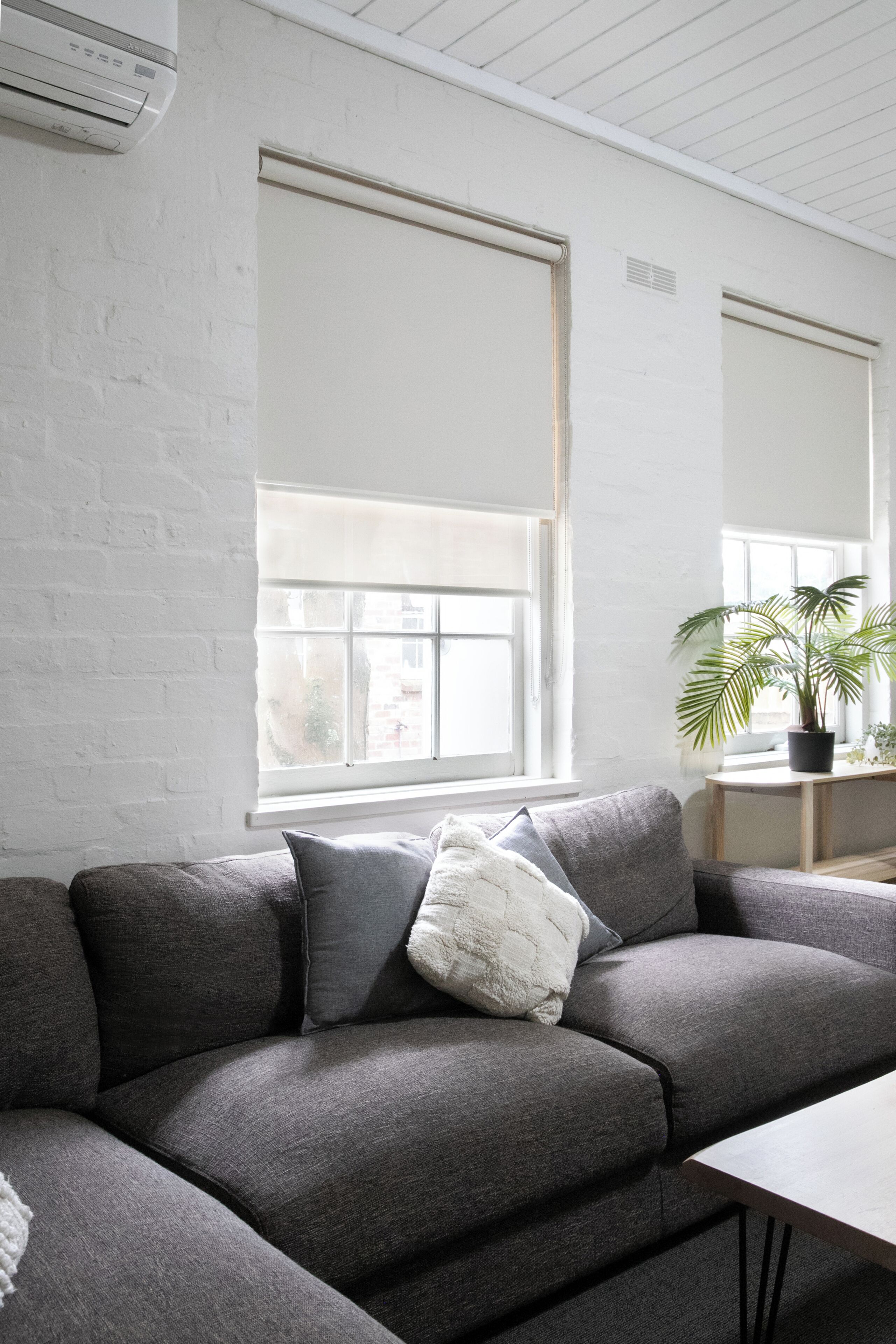 Un salon moderne avec un canapé gris, un mur blanc et une fenêtre avec des stores.