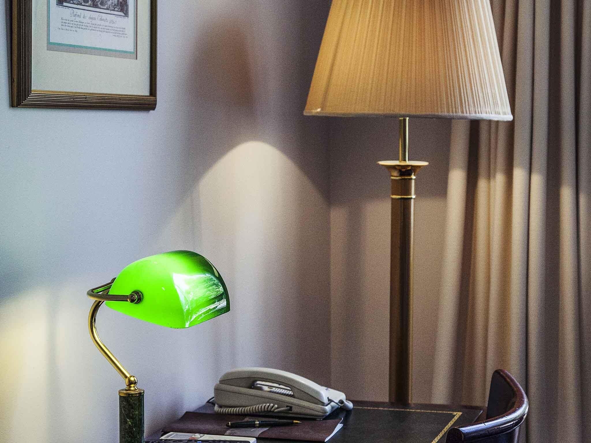 Un escritorio con una lámpara de escritorio verde, un teléfono y un certificado enmarcado en la pared.