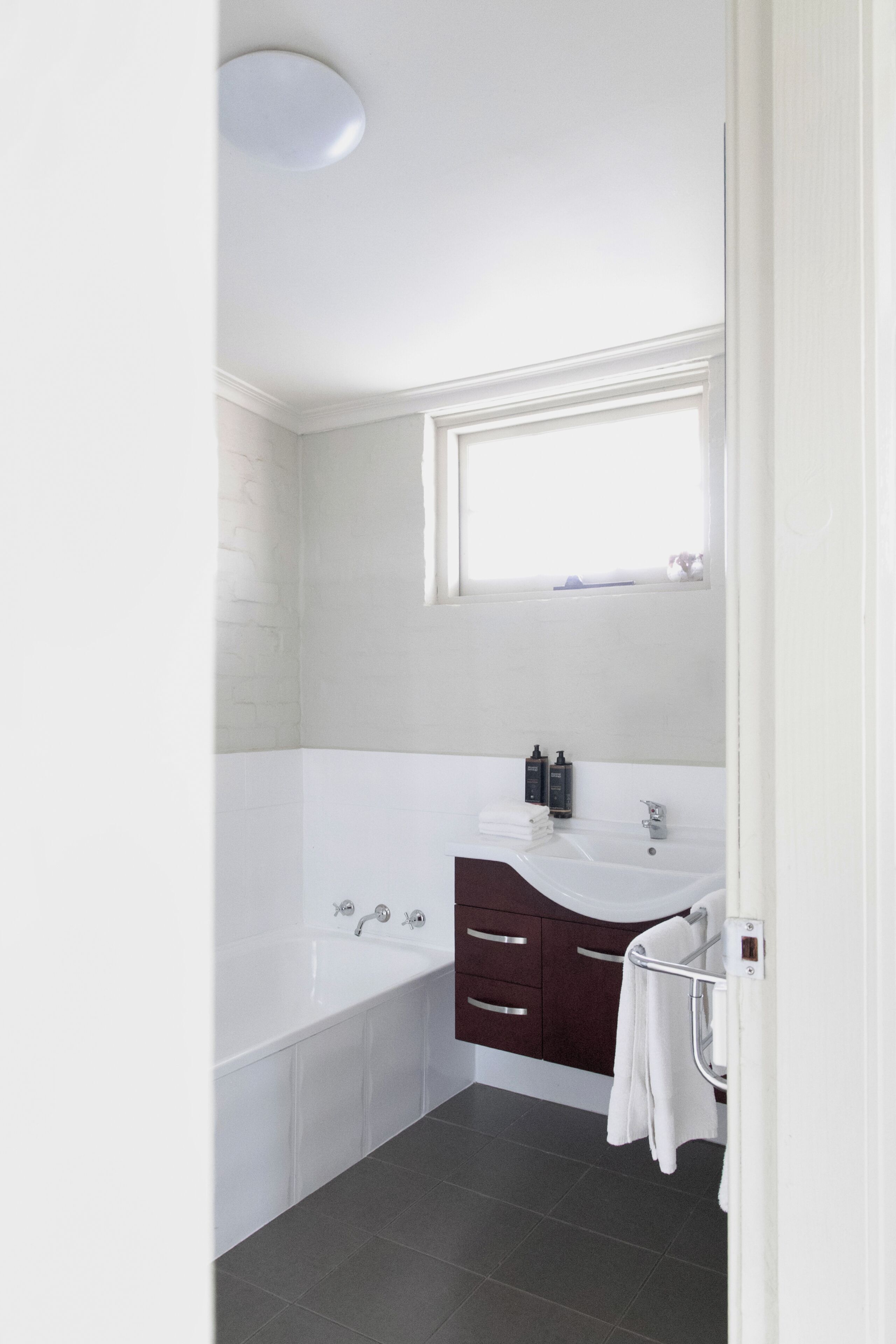 A modern bathroom with a bathtub, a vanity with a mirror, and a window above the sink.