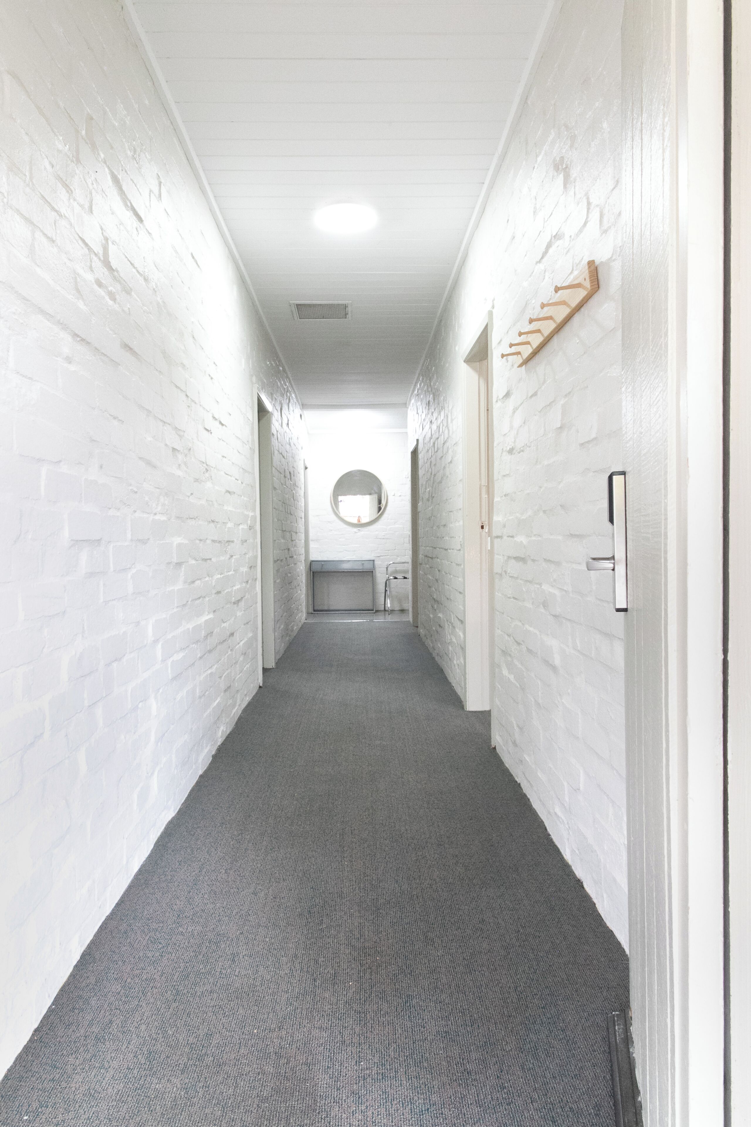 Un pasillo con paredes de ladrillo blanco, alfombra gris y una puerta con perchero de madera.