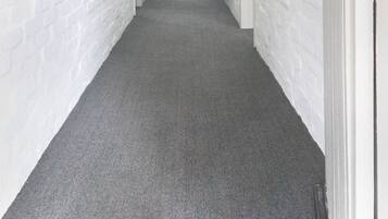 A corridor with white brick walls, a grey carpet, and a door with a wooden coat rack.