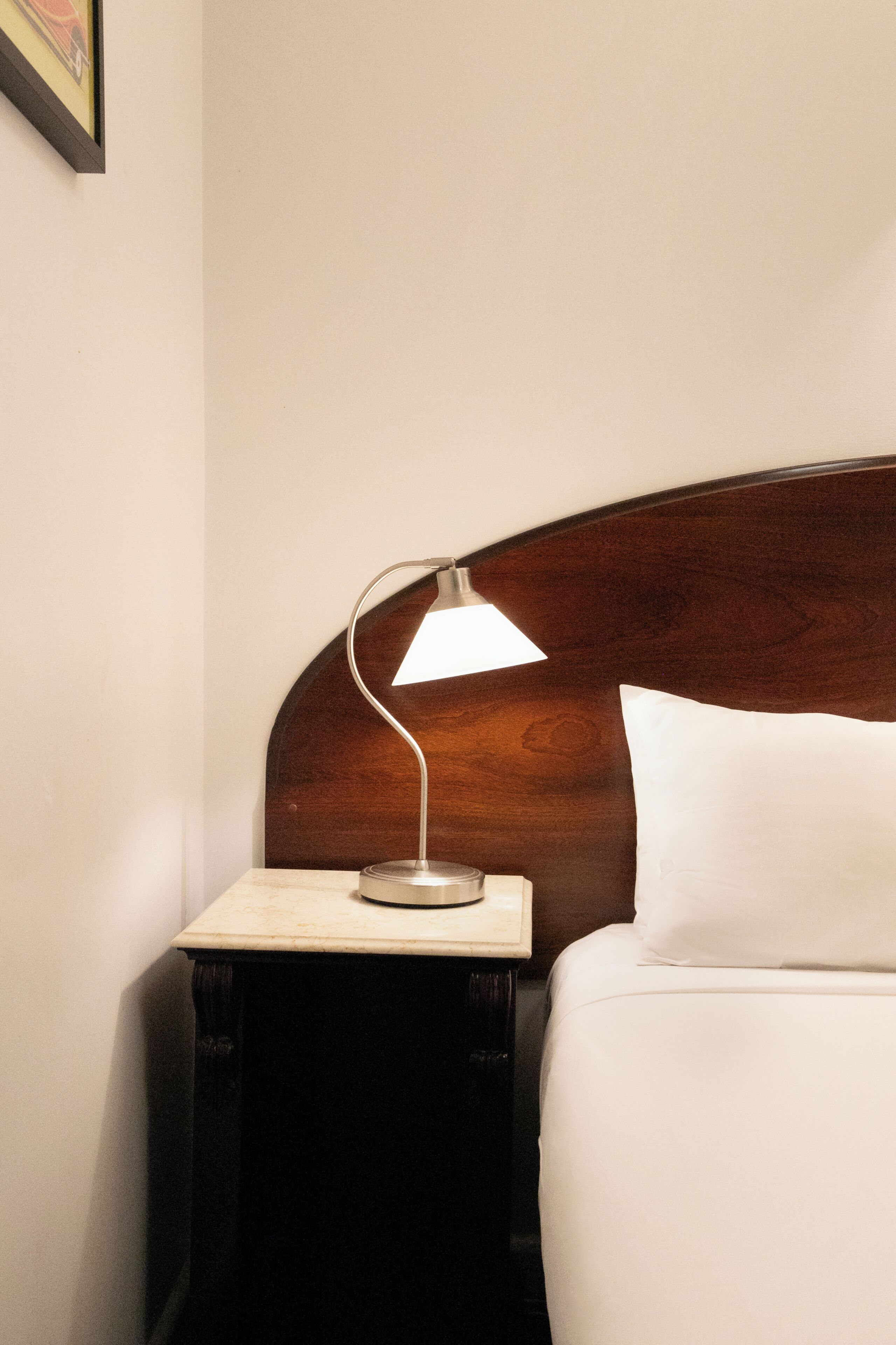 A neatly made bed with a wooden headboard, a bedside table with a lamp, and a framed picture on the wall.