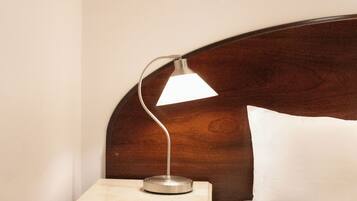 A neatly made bed with a wooden headboard, a bedside table with a lamp, and a framed picture on the wall.