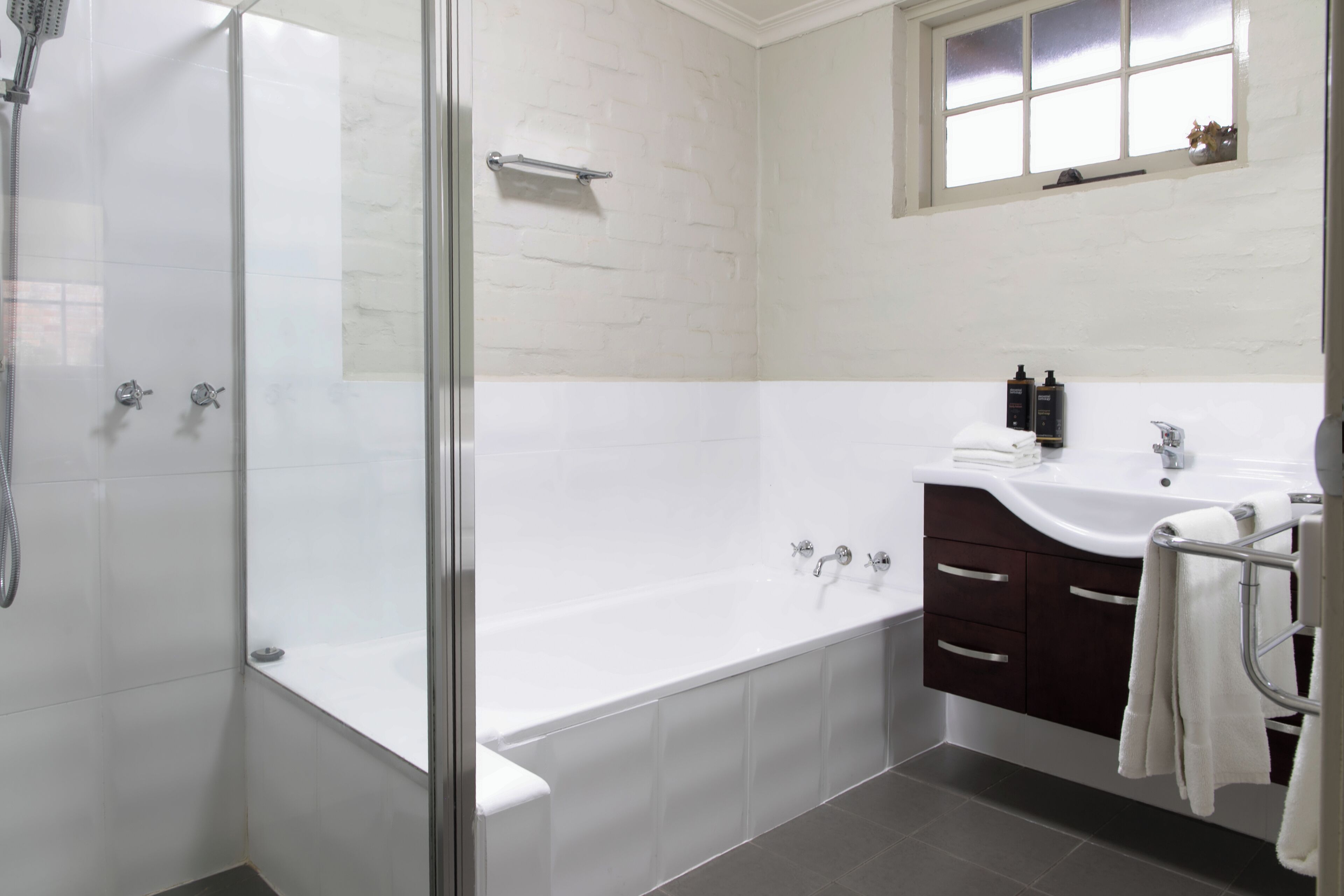 A modern bathroom with a glass-enclosed shower, a freestanding bathtub, a vanity with a sink, and a window above the vanity.