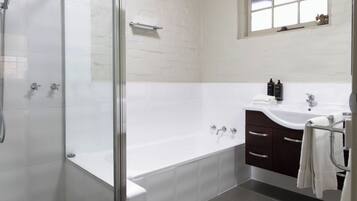 A modern bathroom with a glass-enclosed shower, a freestanding bathtub, a vanity with a sink, and a window above the vanity.