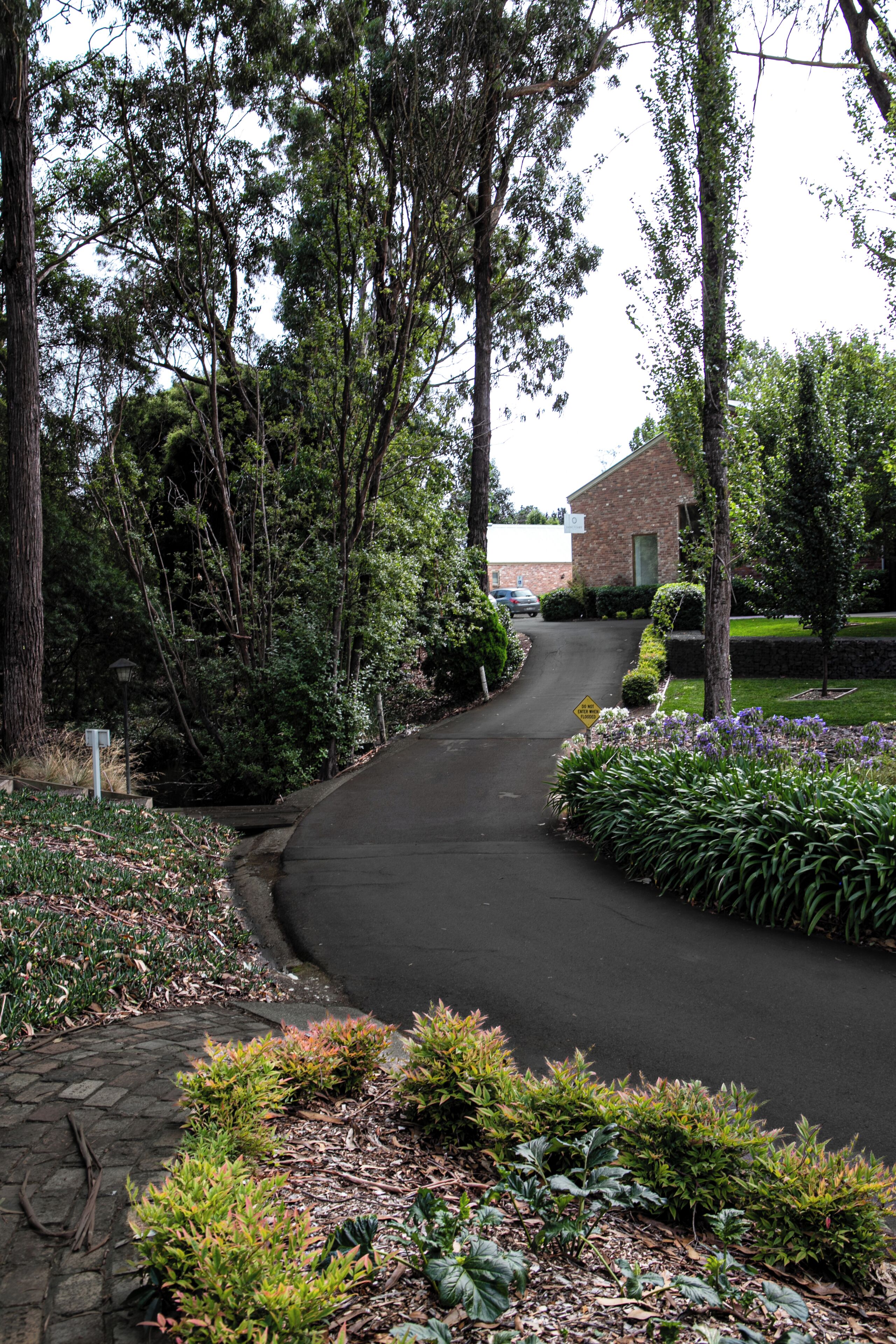 Una calle residencial con un edificio de ladrillo, un camino de entrada y un jardín ajardinado con diversas plantas.