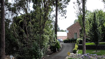 Una calle residencial con un edificio de ladrillo, un camino de entrada y un jardín ajardinado con diversas plantas.