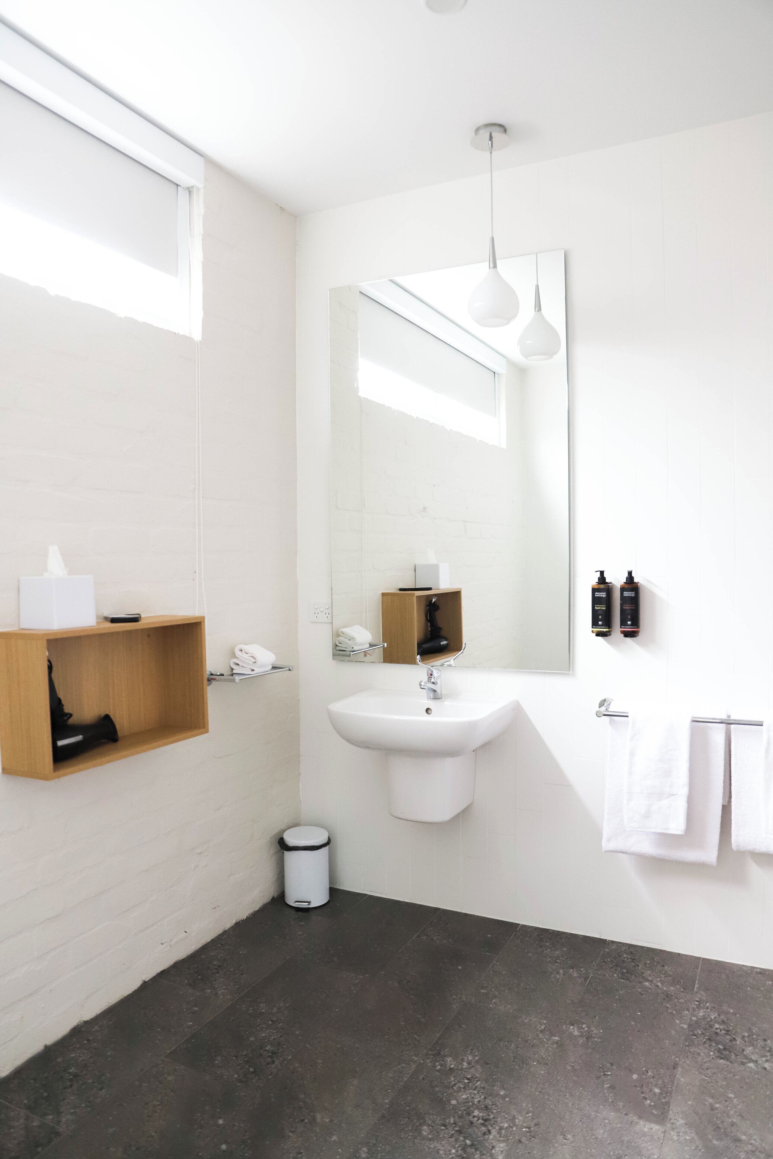 A modern bathroom with a white sink, mirror, and wooden shelf.