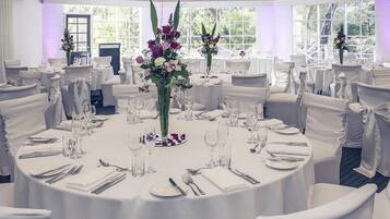 A banquet hall with round tables, white tablecloths, and chairs with white covers.
