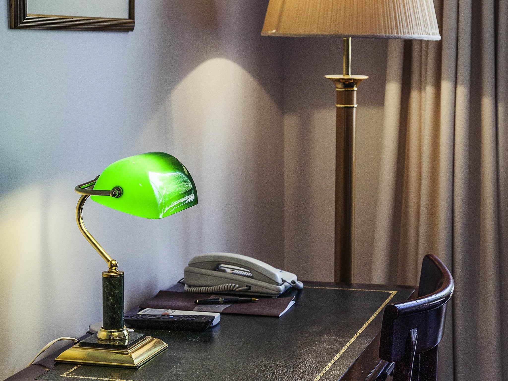 Un bureau avec une lampe de bureau verte, un téléphone, une télécommande et un carnet.
