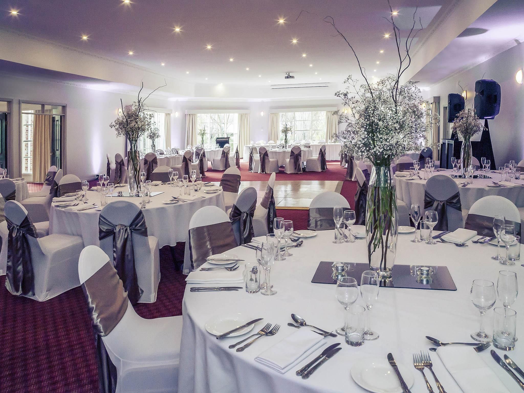 A banquet hall with round tables, chairs, and floral centerpieces.