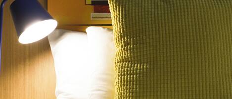A bed with a white pillow and a textured yellow pillow, a blue lamp, and a wall with a cartoon character.