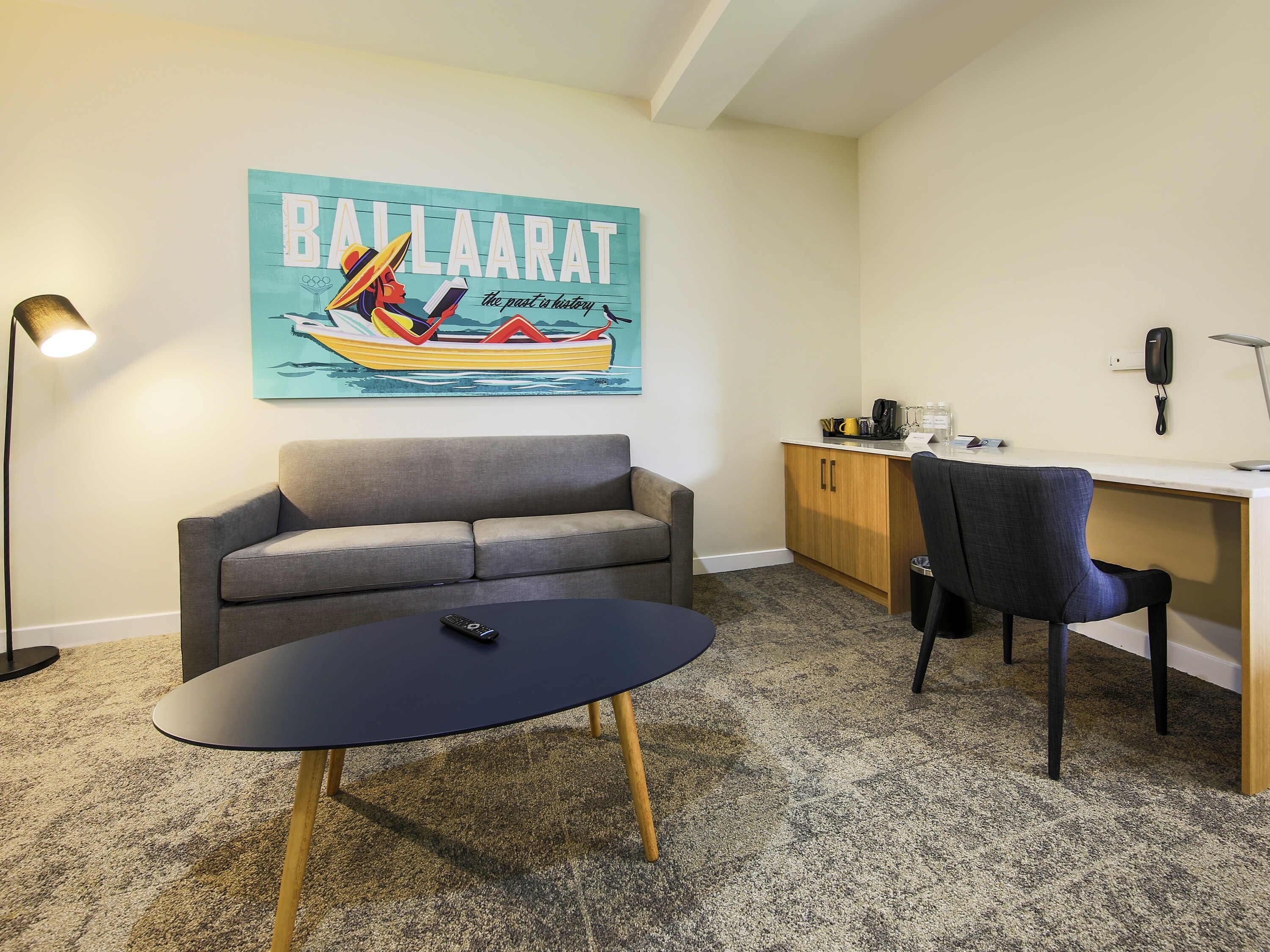 A room with a sofa, a desk, a chair, a table, a lamp, and a wall art piece.