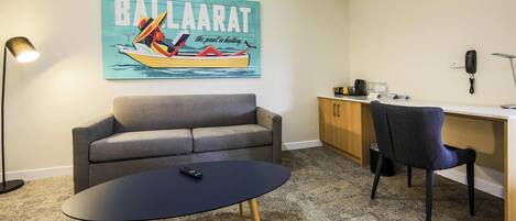 A room with a sofa, a desk, a chair, a table, a lamp, and a wall art piece.