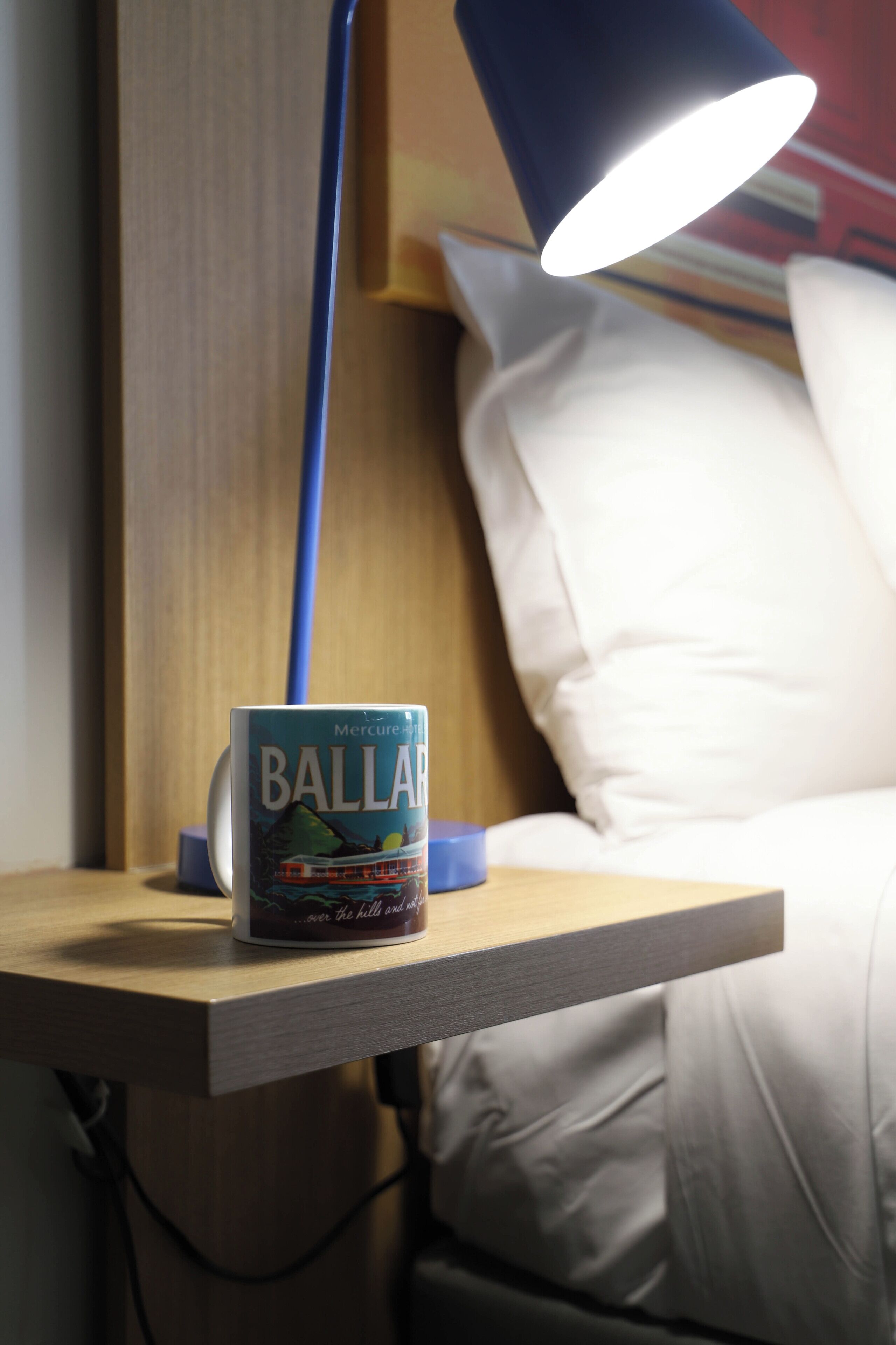 Un libro titulado 'Ballard' sobre una mesita de noche con una lámpara y una cama al fondo.