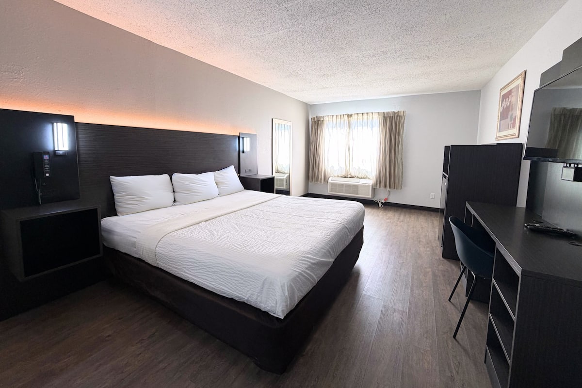 A hotel room with a large bed, a desk with a chair, a TV, and a window with curtains.