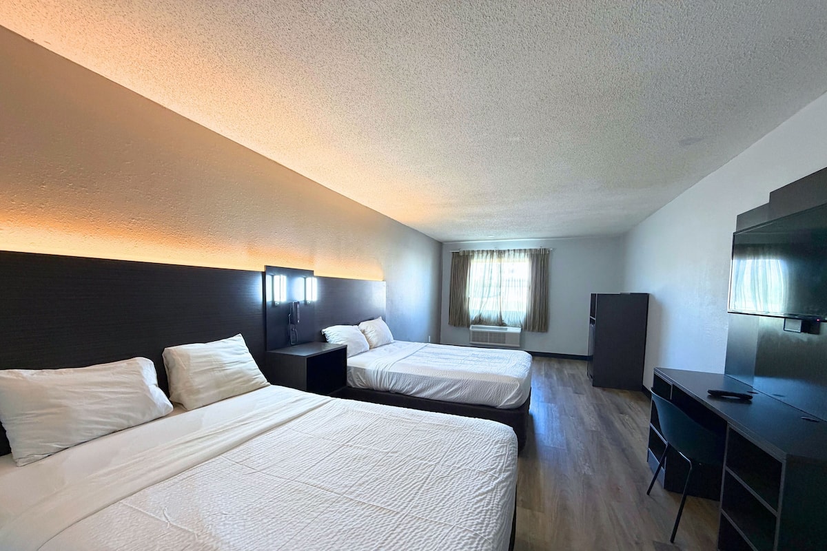 A hotel room with two beds, a desk, a TV, and a window with curtains.