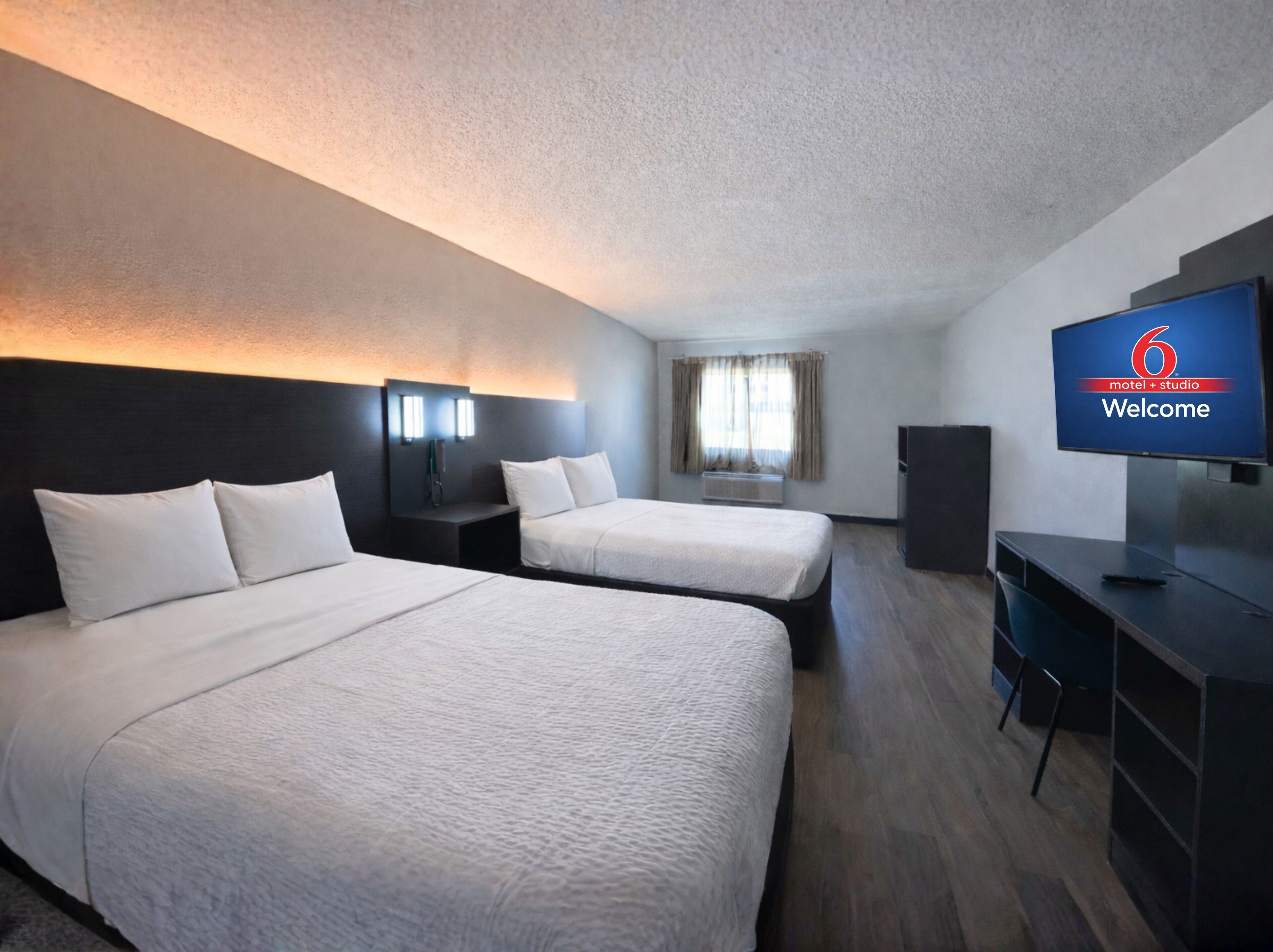 Une chambre d’hôtel avec deux lits, un bureau, une télévision et une fenêtre avec des rideaux.