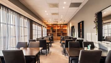 A hotel dining area with tables and chairs, a wooden reception desk, and a large window with curtains.