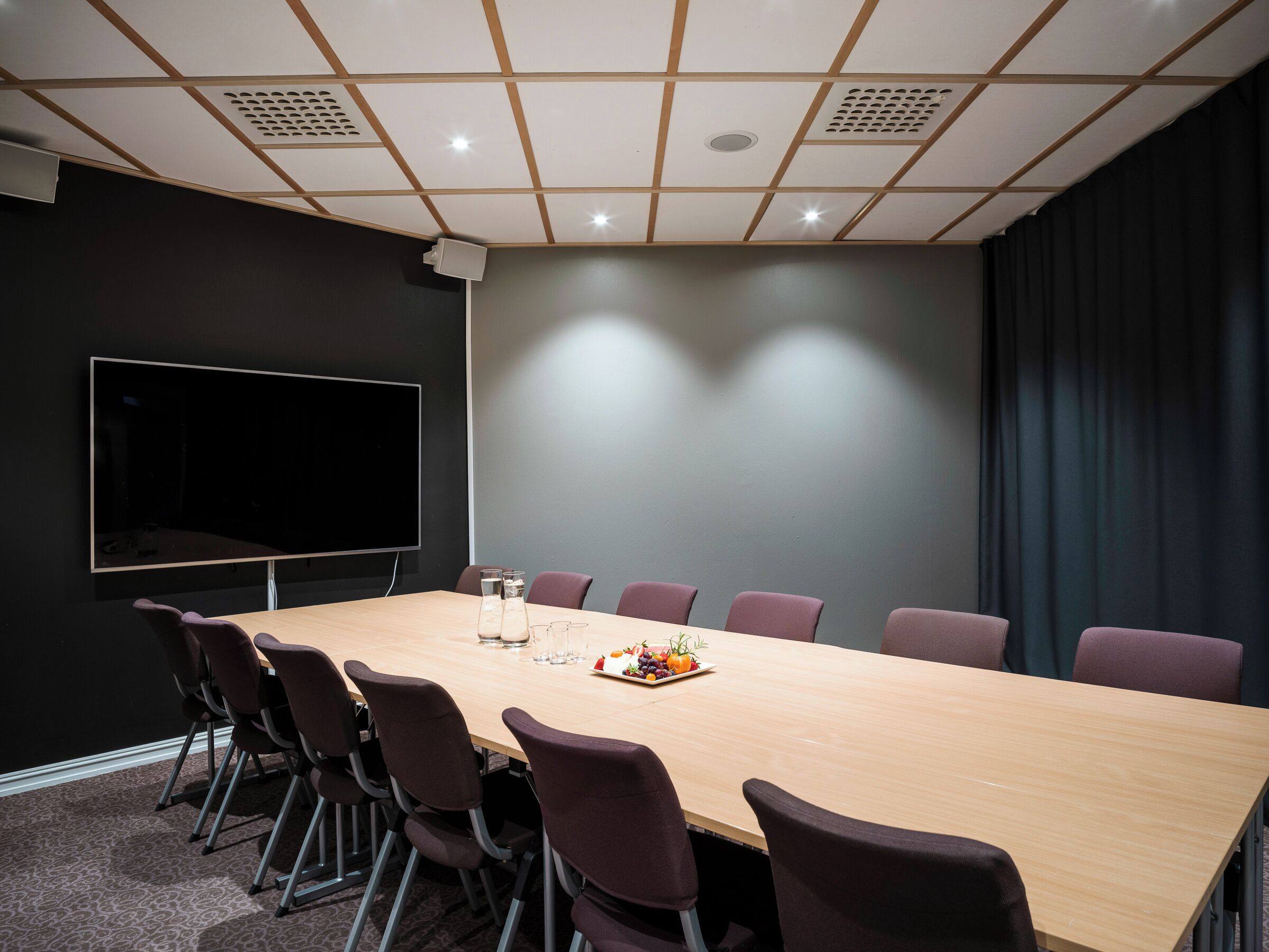 A conference room with a long table, chairs, a flat-screen TV, and a projector.