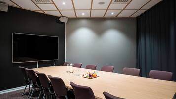 Uma sala de conferências com uma mesa comprida, cadeiras, uma TV de tela plana e um projetor.