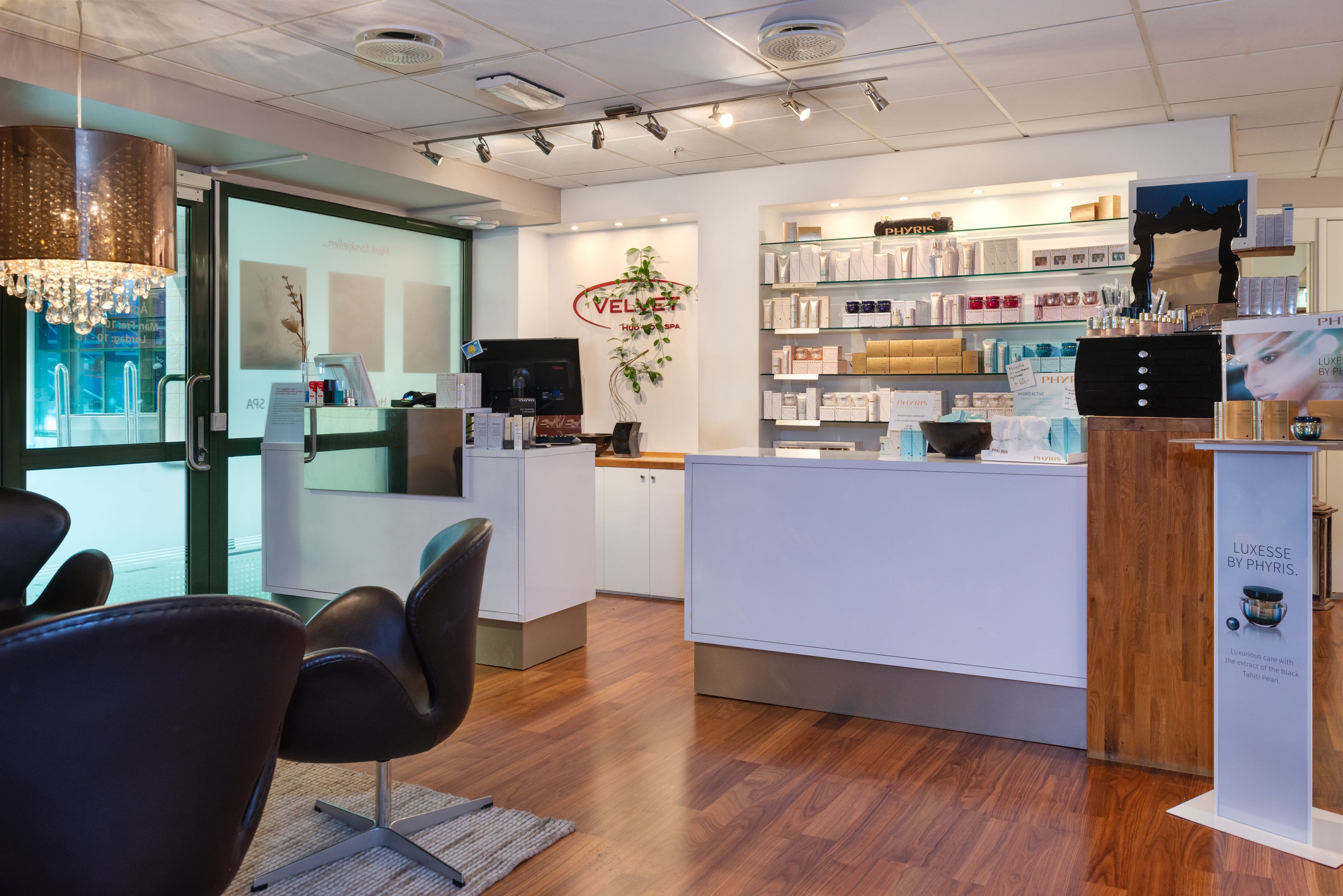 A modern spa interior with a reception desk, wooden flooring, and a variety of spa products on shelves.