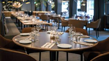 Un restaurante con mesas redondas dispuestas para comer, con copas y platos de vidrio.