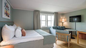 A modern hotel room with a bed, a sofa, a desk, and a TV.