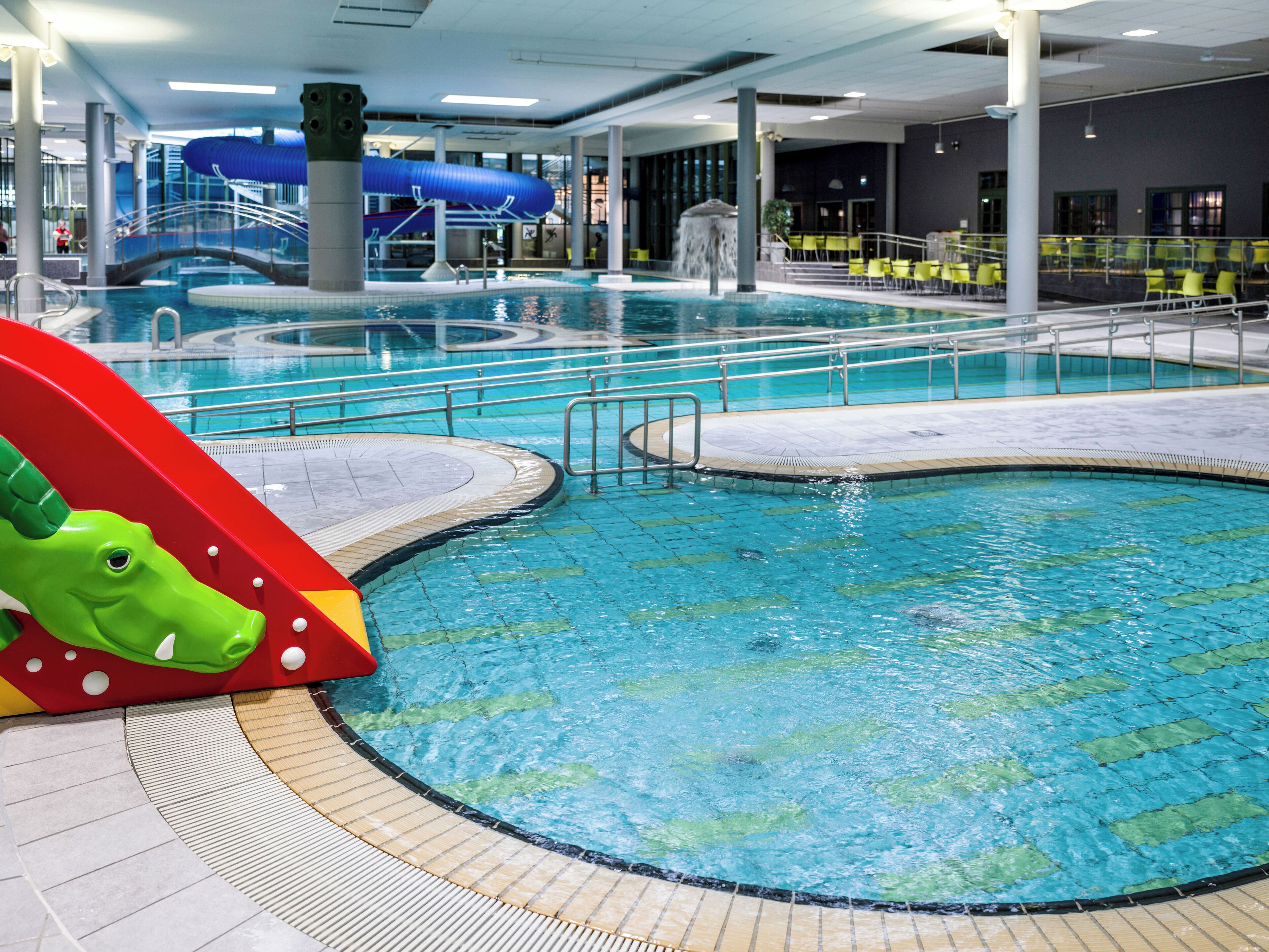 An indoor swimming pool with a slide, multiple lanes, and a water slide in the background.