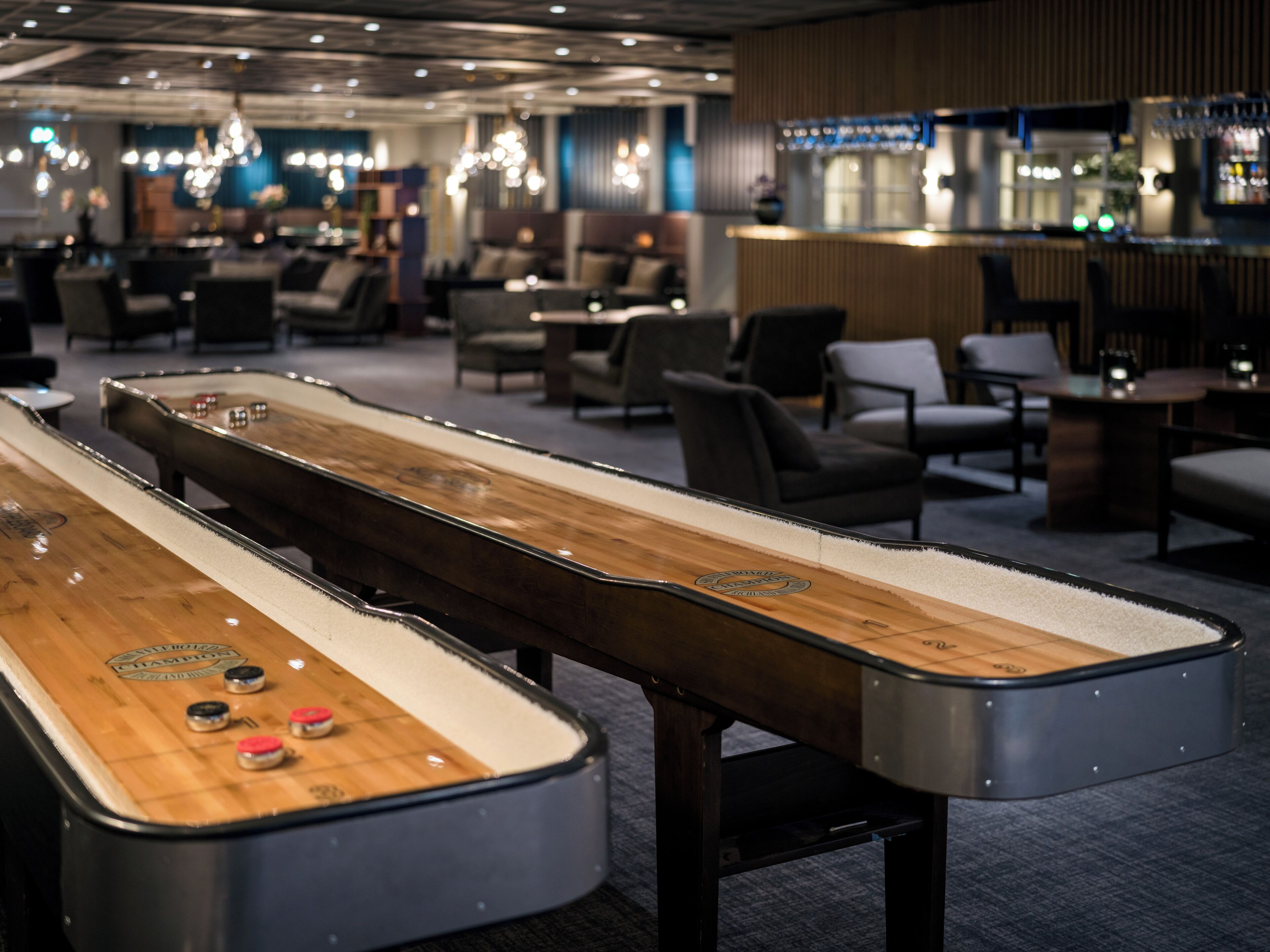 A shuffleboard table in a hotel lobby with seating and a bar area in the background.
