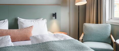 A hotel room with a bed, a chair, a lamp, and a painting on the wall.