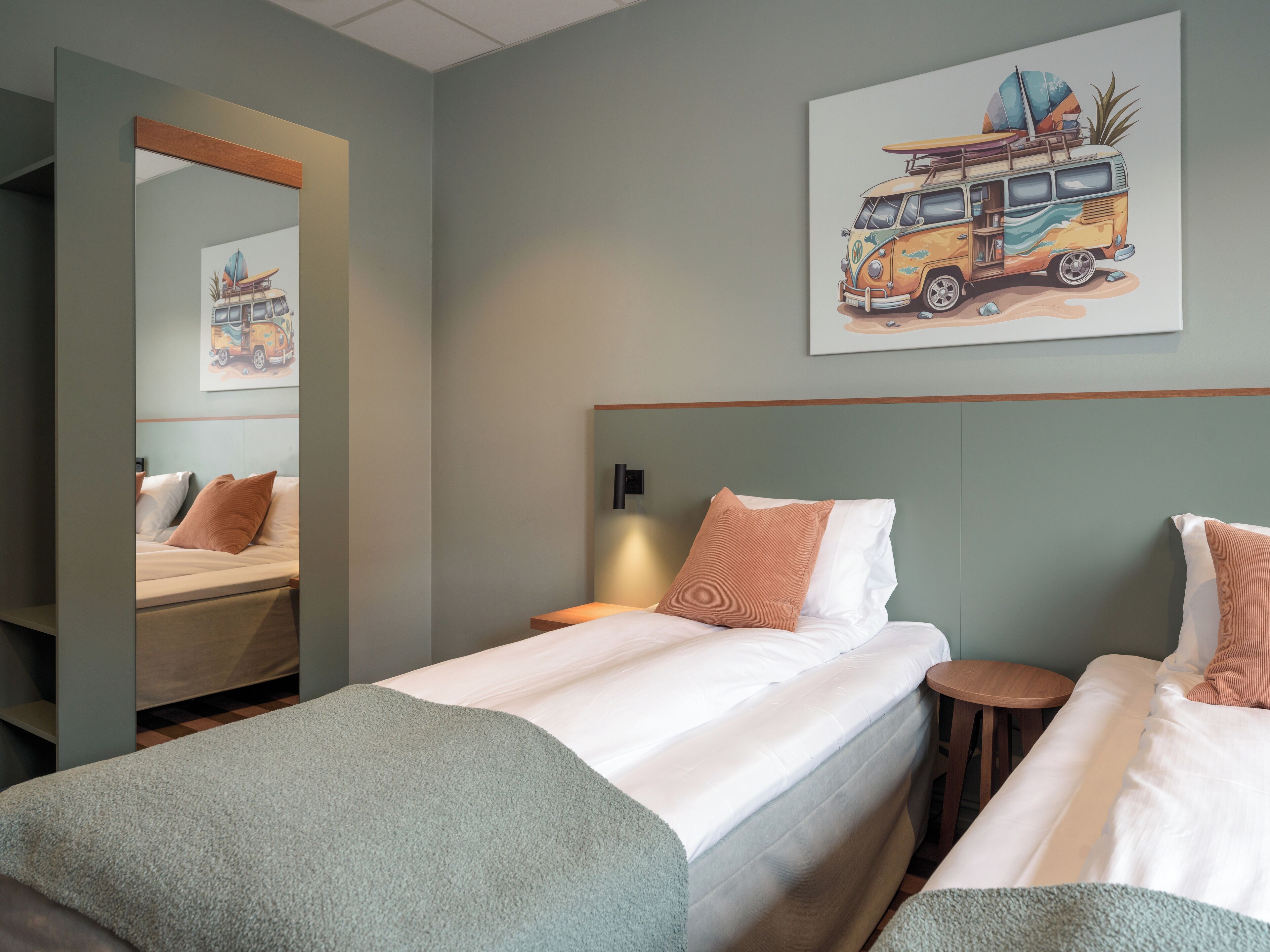 Een hotelkamer met een bed, een nachtkastje, een spiegel en een aan de muur hangend kunstwerk van een busje.