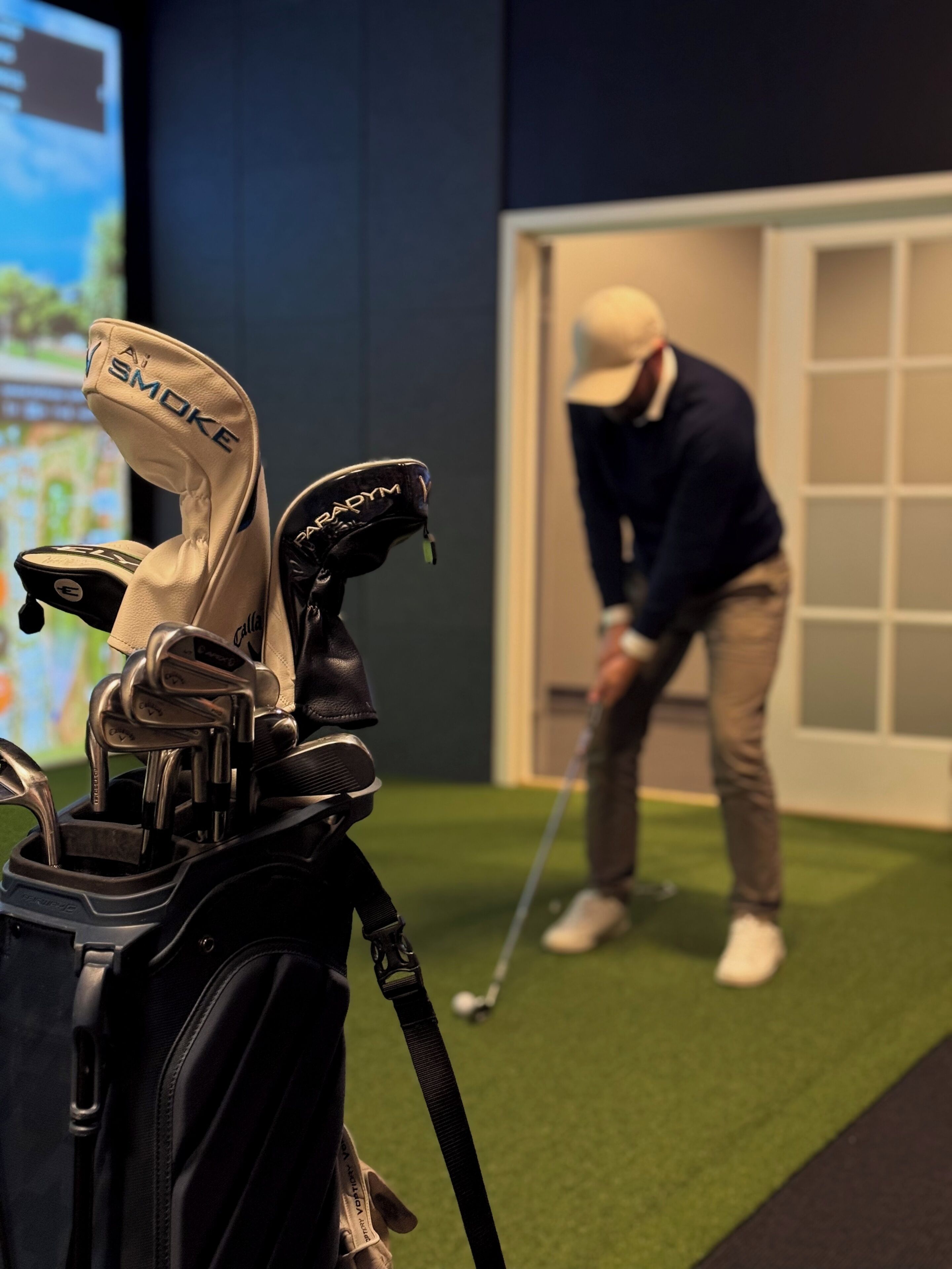 Un bolso de golf con palos y una persona jugando golf al fondo.