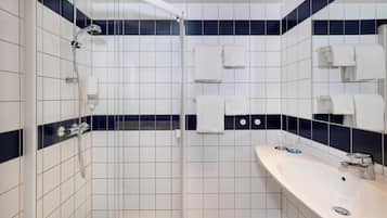 Un baño con ducha envuelta en vidrio, un lavabo blanco y varias toallas.