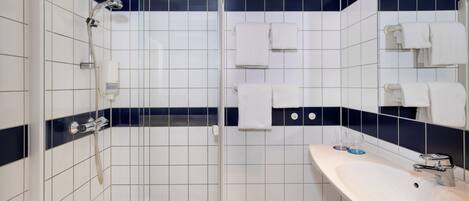 A bathroom with a glass-enclosed shower, a white sink, and multiple towels.