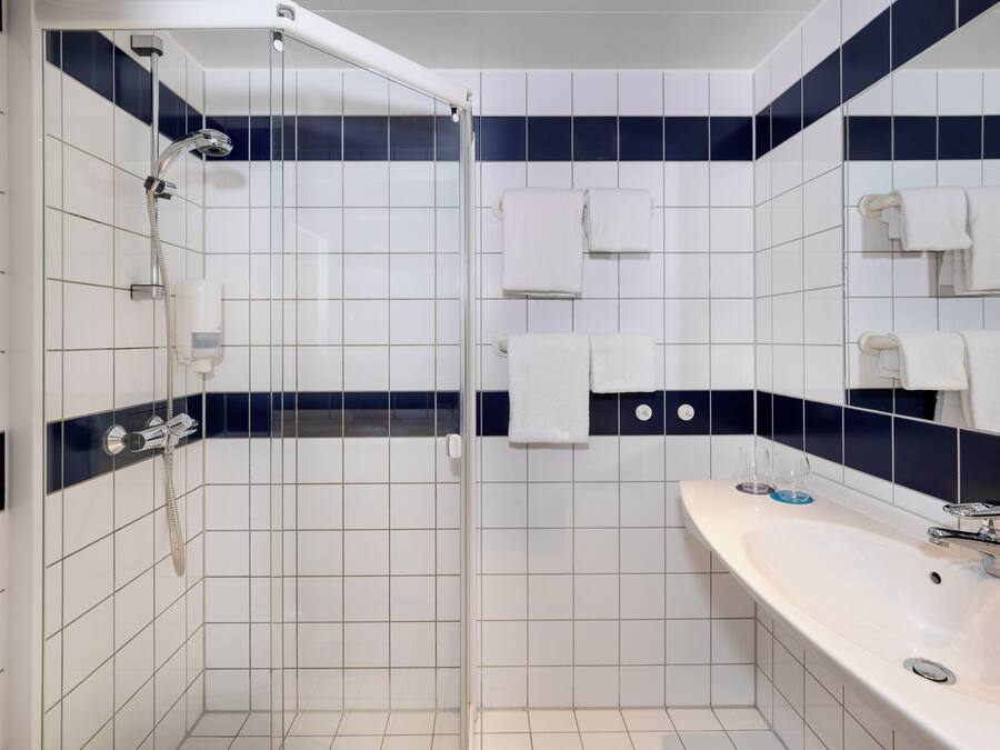 Un baño con ducha envuelta en vidrio, un lavabo blanco y varias toallas.