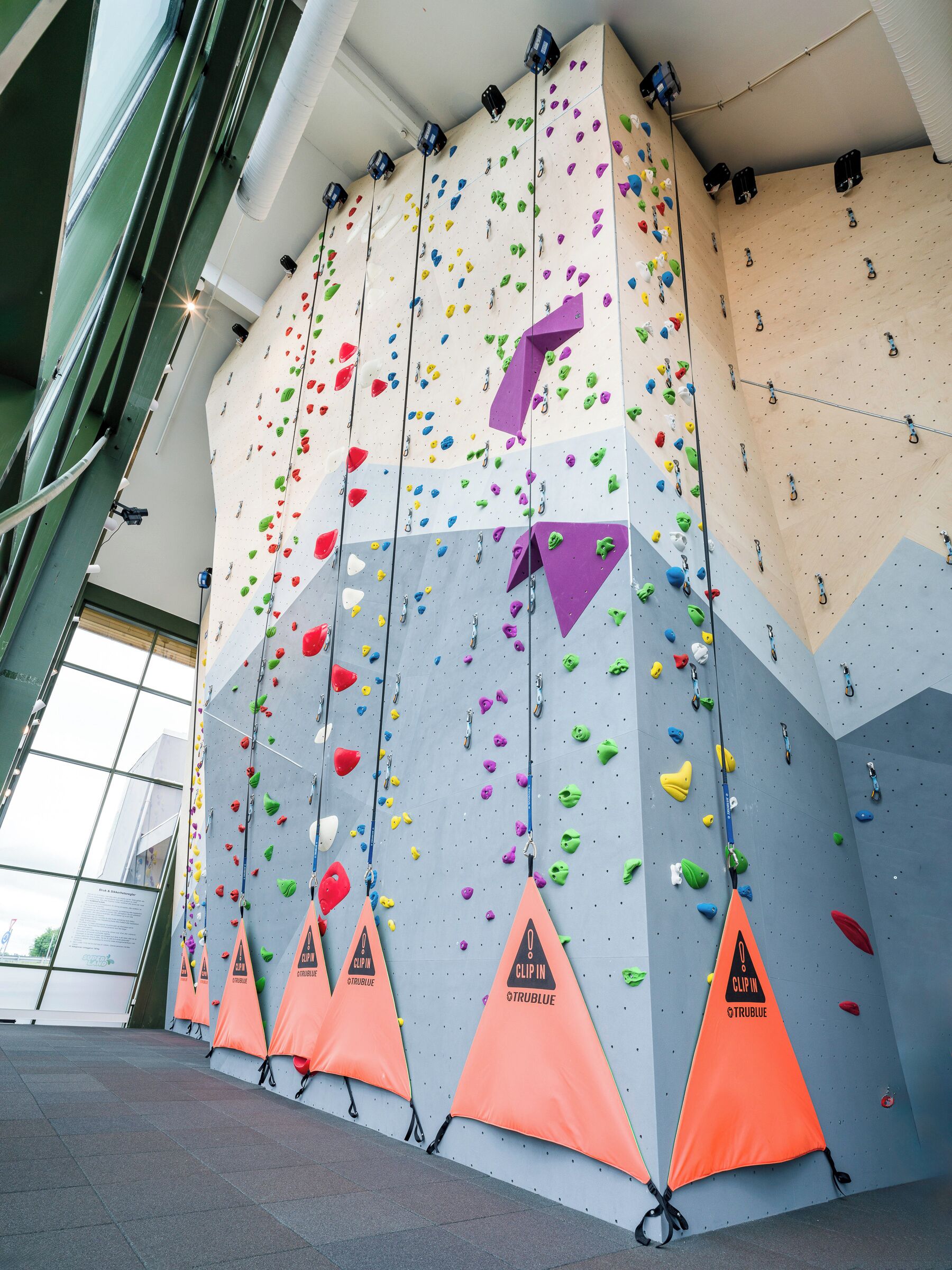 Una pared de escalada con varias rutas, conos de seguridad y puntos de agarre.