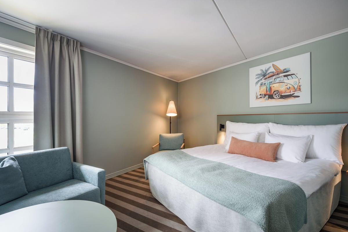 Habitación de hotel con una cama grande, una silla, una mesita y una lámpara.