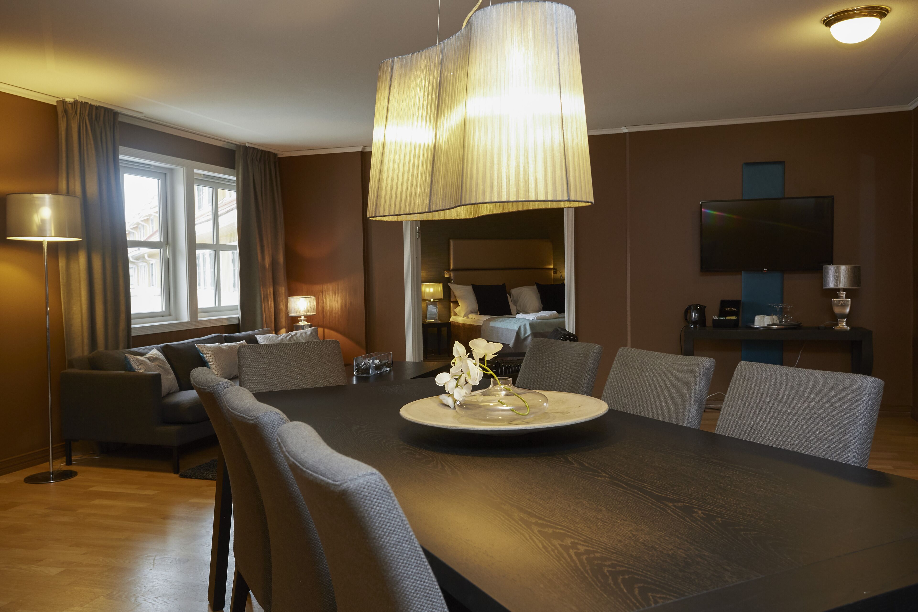 Une chambre d’hôtel moderne dotée d’un coin repas, d’un canapé, d’une télévision et d’une grande fenêtre.
