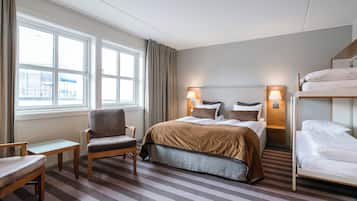 A hotel room with a bed, a chair, a desk, and a window with curtains.