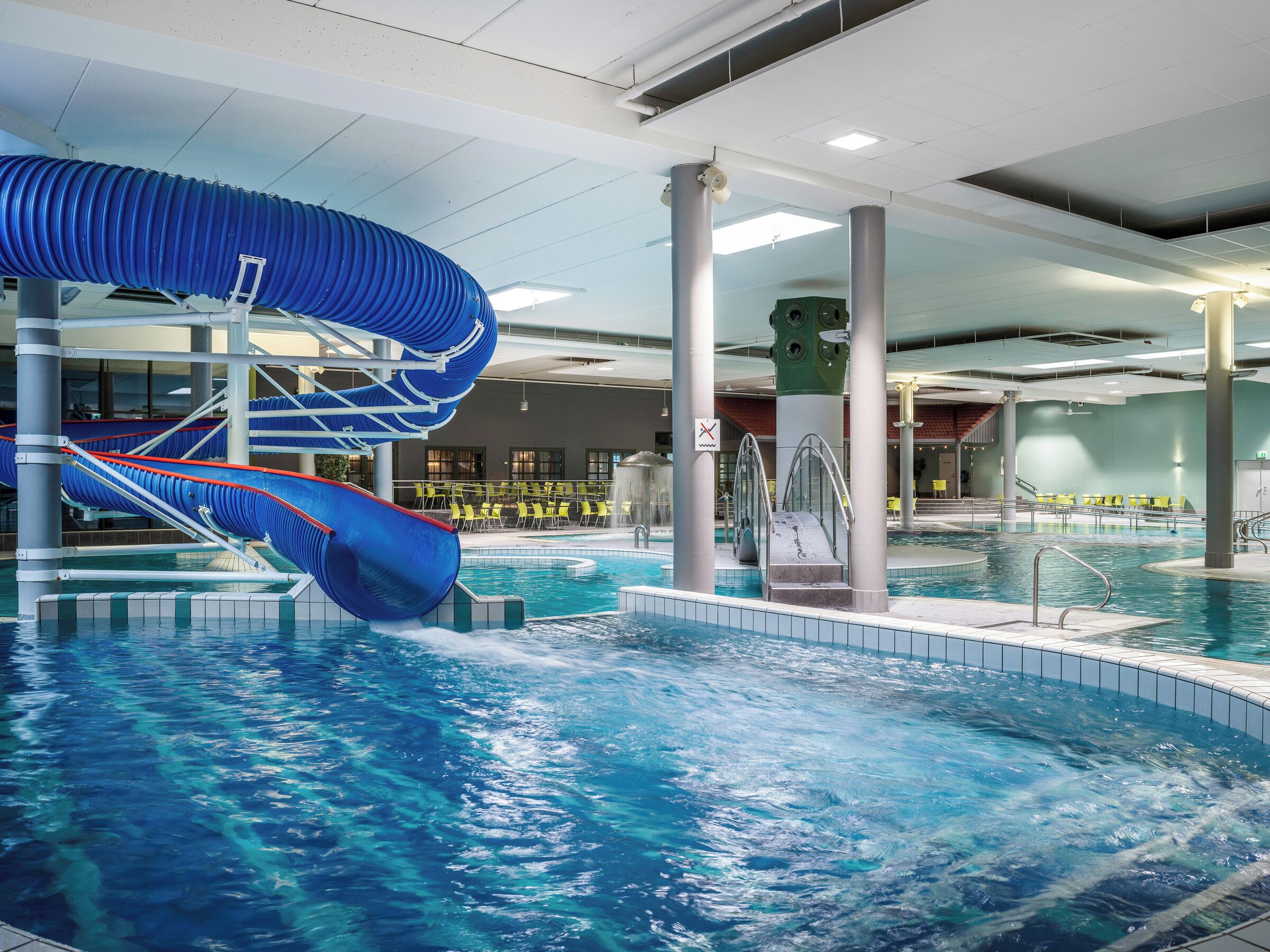 An indoor swimming pool with a blue water slide and a diving platform.