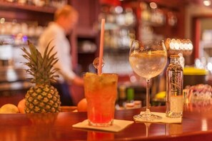 Un bar con una piña, un vaso de cóctel rojo y una botella de licor sobre la barra.