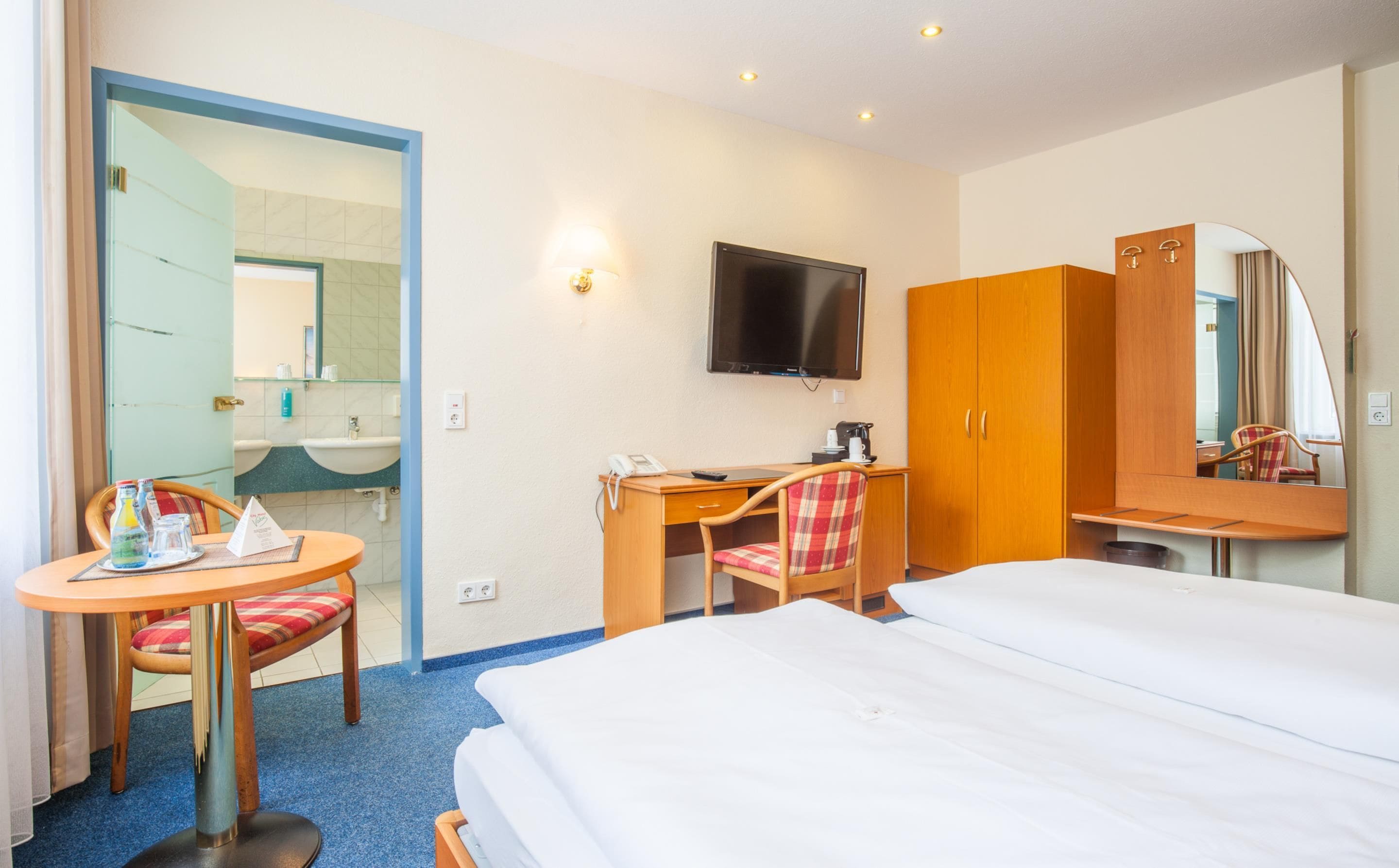 A hotel room with a bed, a desk, a chair, a television, and a wardrobe.