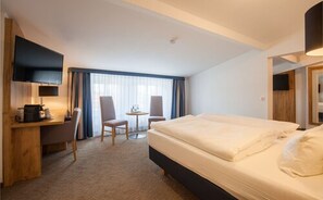 A hotel room with a bed, a desk, a chair, a small table, and a TV.