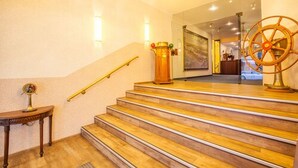 Una escalera de madera con barandilla que lleva a una habitación con candelabro y timón de barco.