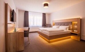 Une chambre d’hôtel avec un grand lit, un bureau avec une chaise, une télévision et une fenêtre avec des rideaux.